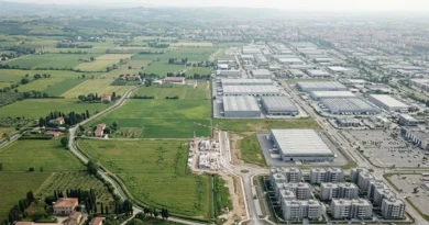 Veduta aerea del consumo di suolo in Italia, con nuove aree residenziali e capannoni che sostituiscono campi agricoli.