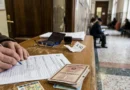 Mano che compila il modulo di richiesta del certificato dei carichi pendenti con la carta d'identità nel corridoio di una Procura